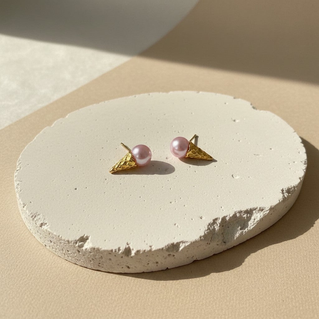 Findingyoyo Gelato earrings featuring pink pearl scoops on textured gold ice cream cones on a stone display base.